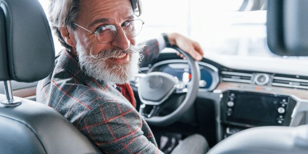 Positive stylish senior man with grey hair and mustache looks back in the modern car.
